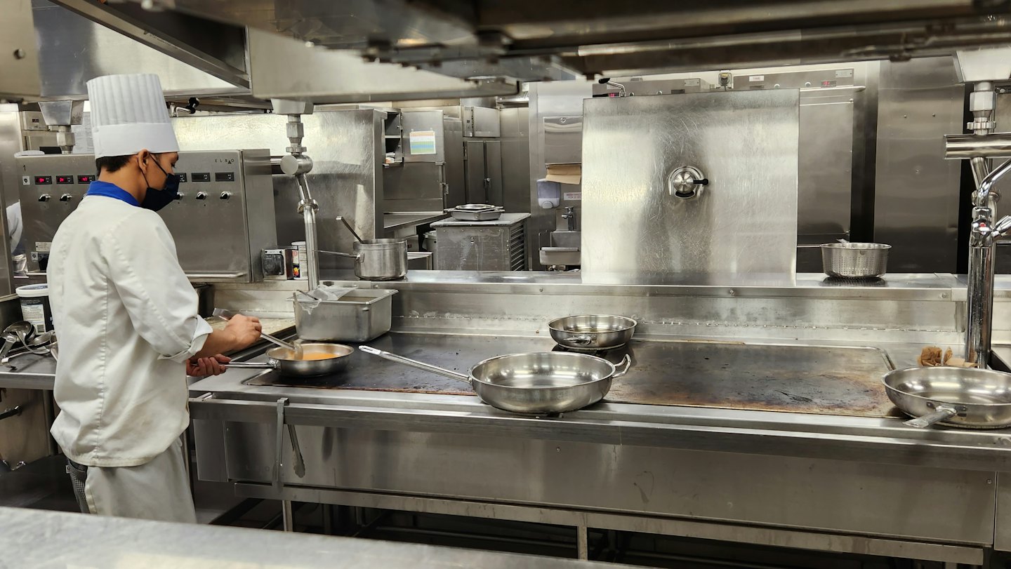 Chef in a mask stirs food on a commercial grill.